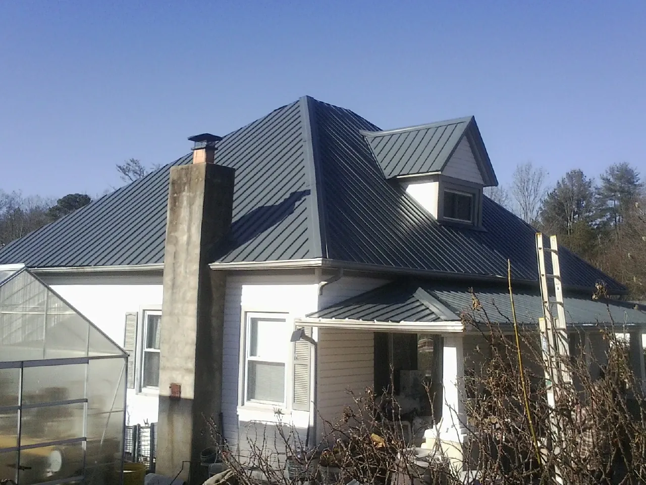 Dark blue standing seam metal roof on a white farmhouse with dormer — Slate & Tile Roof Repair by Roofing Brothers in Huntington Woods