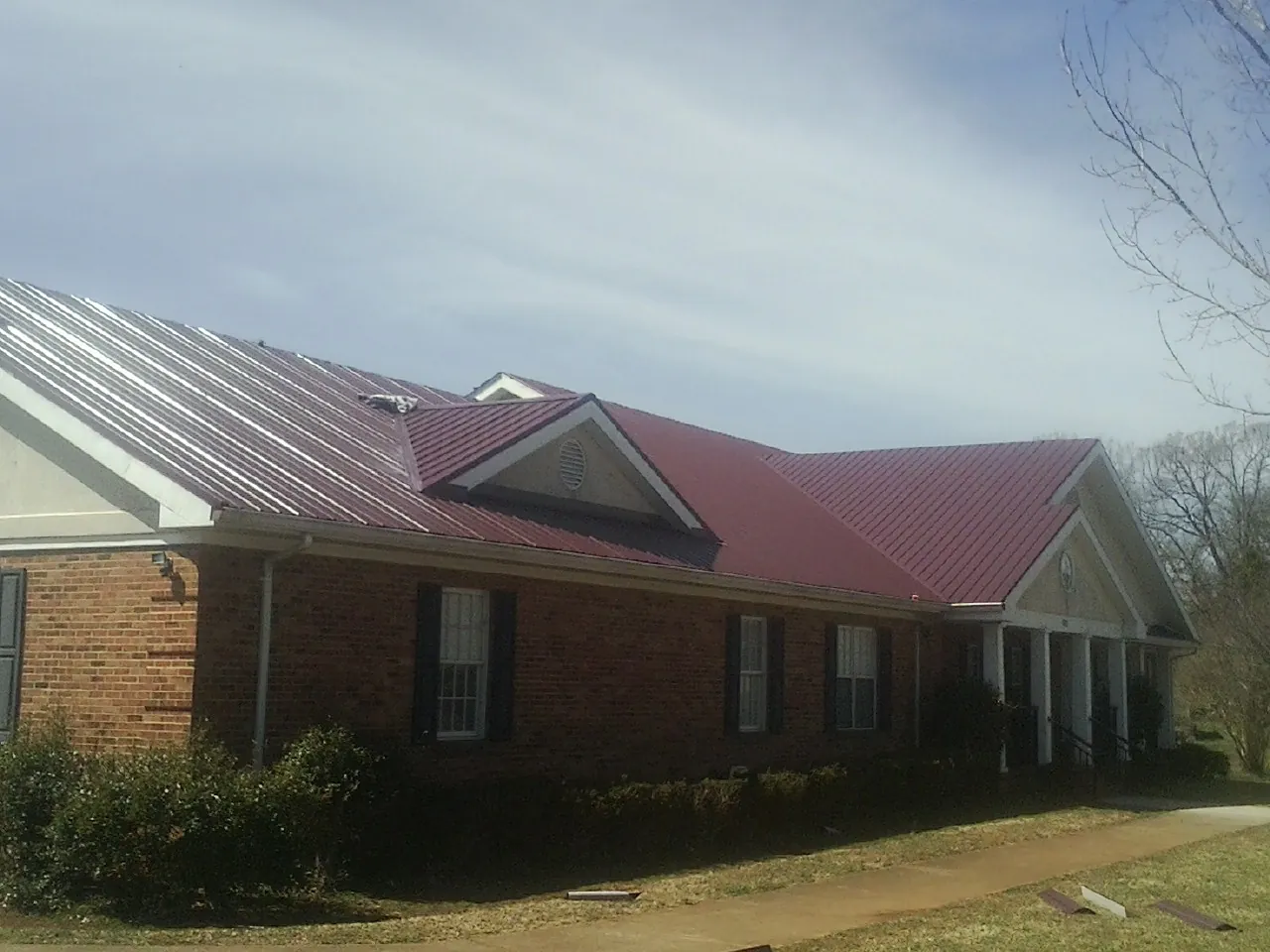 Red metal roof with gabled entries on a long brick building, from a Hail Damage Roof Repair job in Huntington Woods