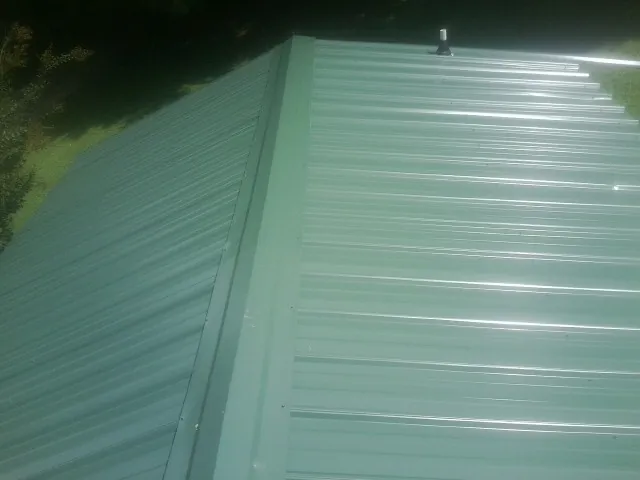 New green metal panels meeting at the ridge of a roof — Flat Roof Repair work by our crew in Huntington Woods