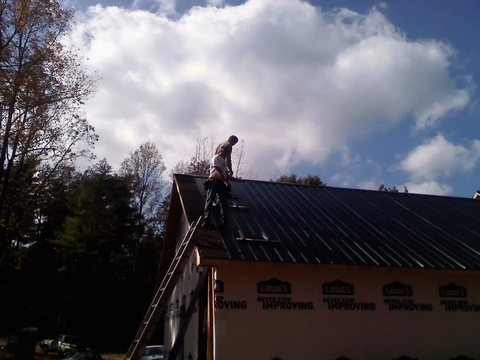 Roofer fastening dark metal panels high against a cloudy sky, from a Roof Inspection job in Huntington Woods