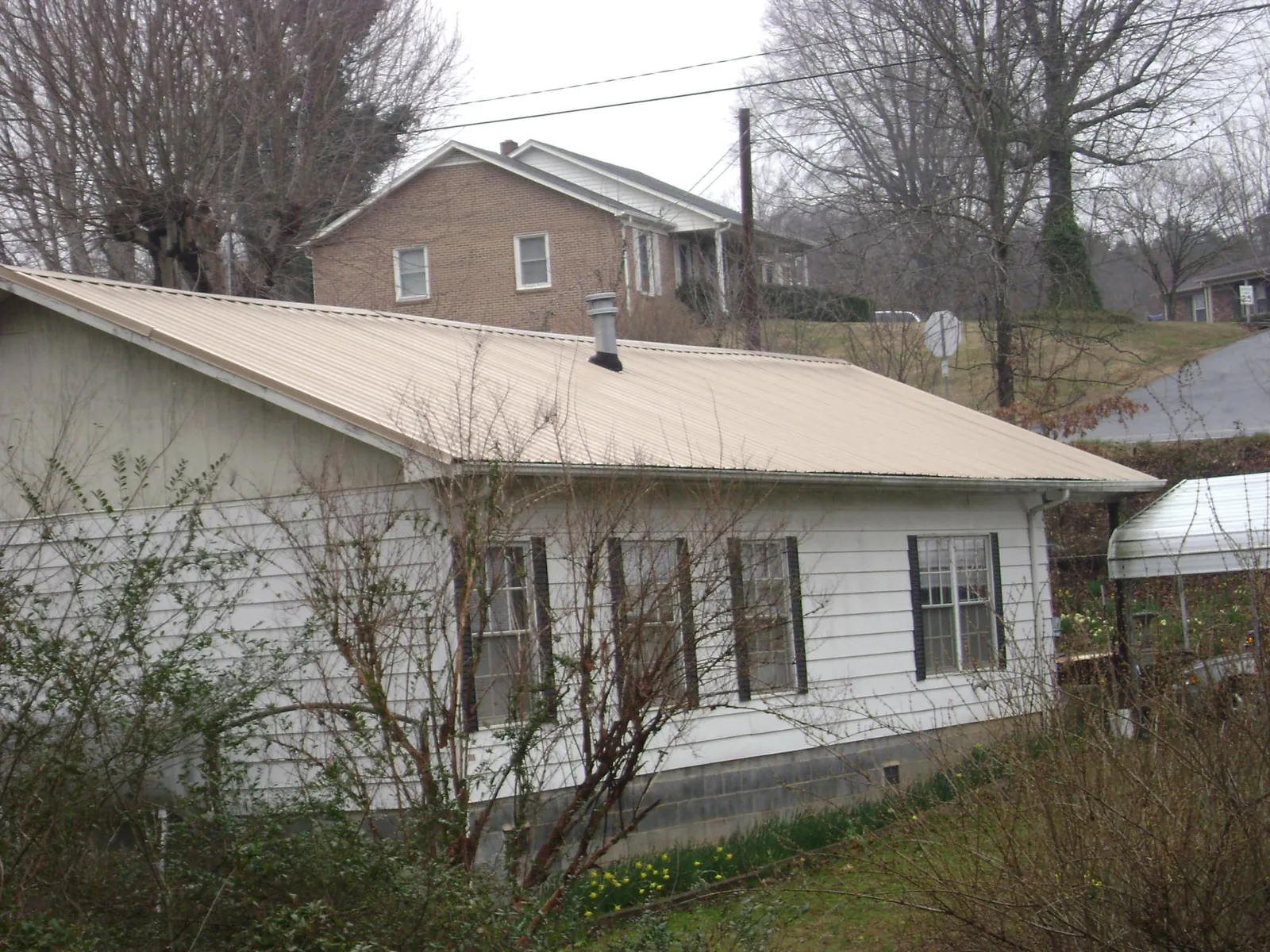 Tan metal roof on a white sided house set into a hillside — Commercial Roofing by Roofing Brothers in Huntington Woods
